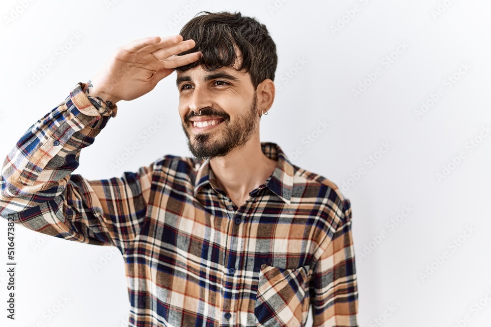 Hispanic man with beard standing over isolated background very happy and smiling looking far away with hand over head. searching concept. Hispanic man with beard standing over isolated background very happy and smiling looking far away with hand over head. searching concept.
