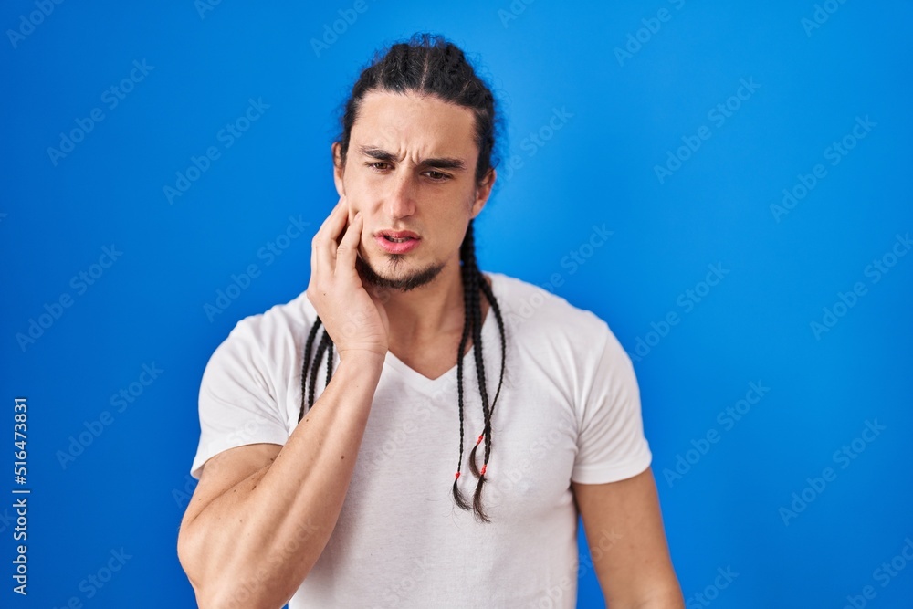 Hispanic man with long hair standing over blue background touching mouth with hand with painful expression because of toothache or dental illness on teeth. dentist Hispanic man with long hair standing over blue background touching mouth with hand with painful expression because of toothache or dental illness on teeth. dentist