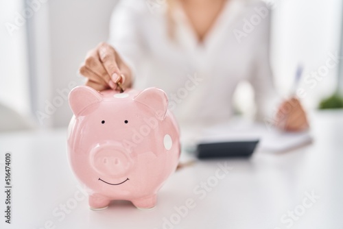 Fotografia Young woman inserting coin on piggy bank at home