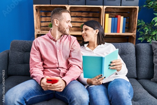 Man and woman couple using smartphone reading book at home