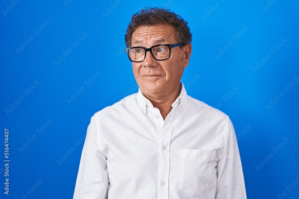Middle age hispanic man standing over blue background smiling looking to the side and staring away thinking. Middle age hispanic man standing over blue background smiling looking to the side and staring away thinking.