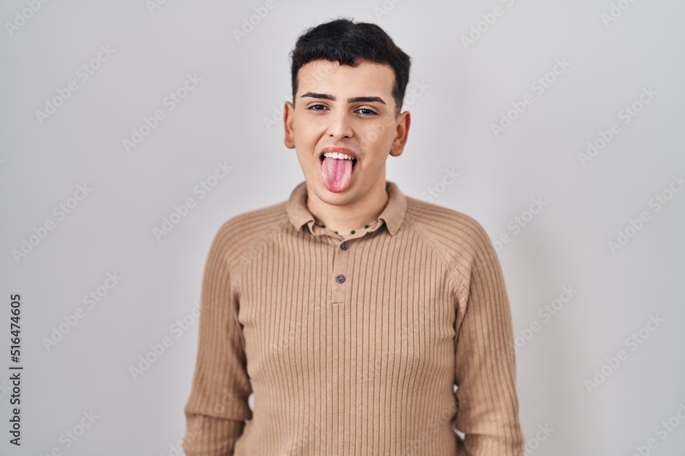 Non binary person standing over isolated background sticking tongue out happy with funny expression. emotion concept. Non binary person standing over isolated background sticking tongue out happy with funny expression. emotion concept.
