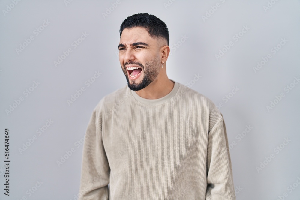 Young handsome man standing over isolated background angry and mad screaming frustrated and furious, shouting with anger. rage and aggressive concept. Young handsome man standing over isolated background angry and mad screaming frustrated and furious, shouting with anger. rage and aggressive concept.