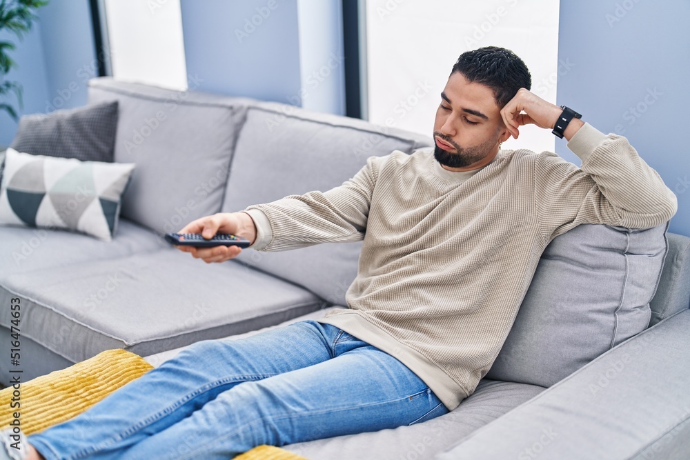 Young arab man watching tv with boring expression at home
