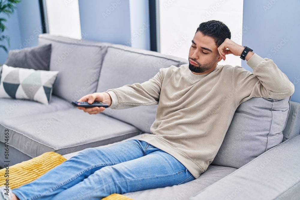 Young arab man watching tv with boring expression at home Young arab man watching tv with boring expression at home