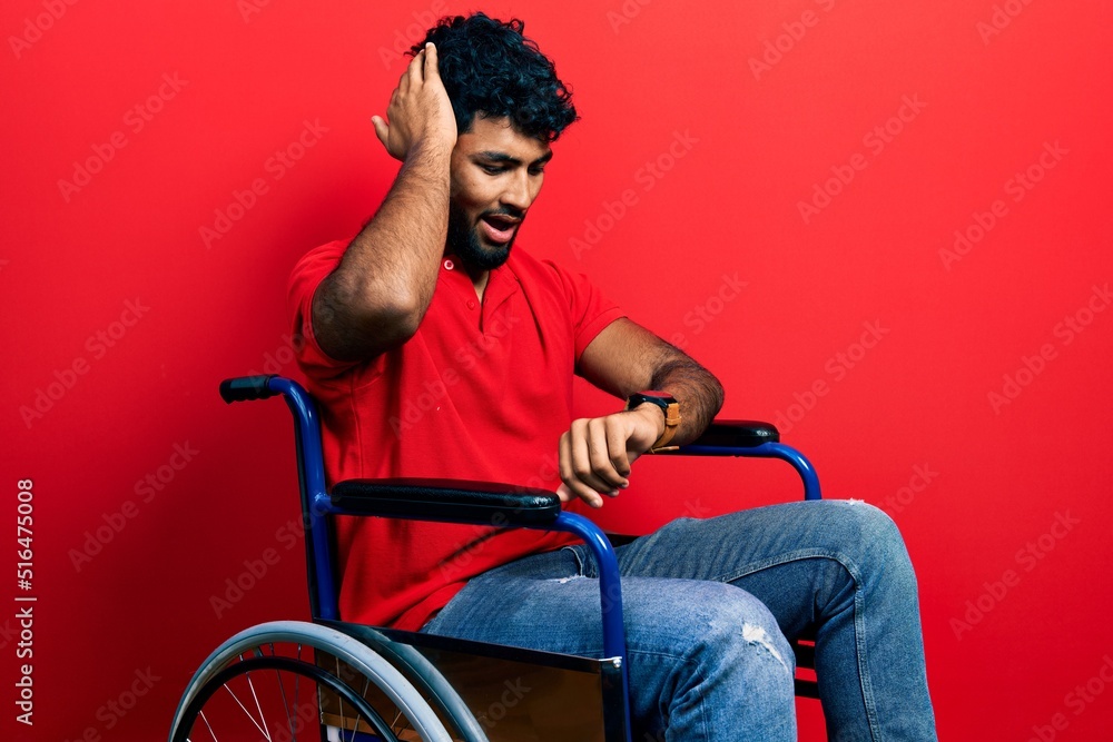 Arab man with beard sitting on wheelchair looking at the watch time worried, afraid of getting late Arab man with beard sitting on wheelchair looking at the watch time worried, afraid of getting late
