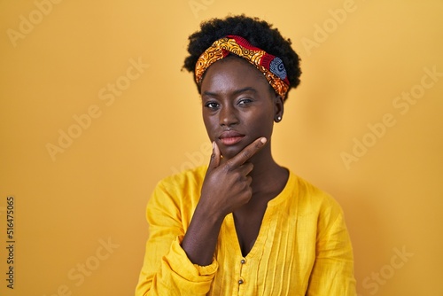 African young woman wearing african turban looking confident at the camera with smile with crossed arms and hand raised on chin. thinking positive.