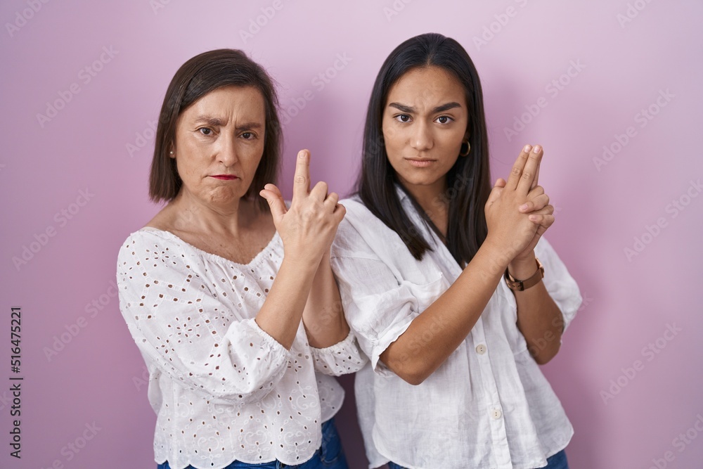 Hispanic mother and daughter together holding symbolic gun with hand gesture, playing killing shooting weapons, angry face Hispanic mother and daughter together holding symbolic gun with hand gesture, playing killing shooting weapons, angry face