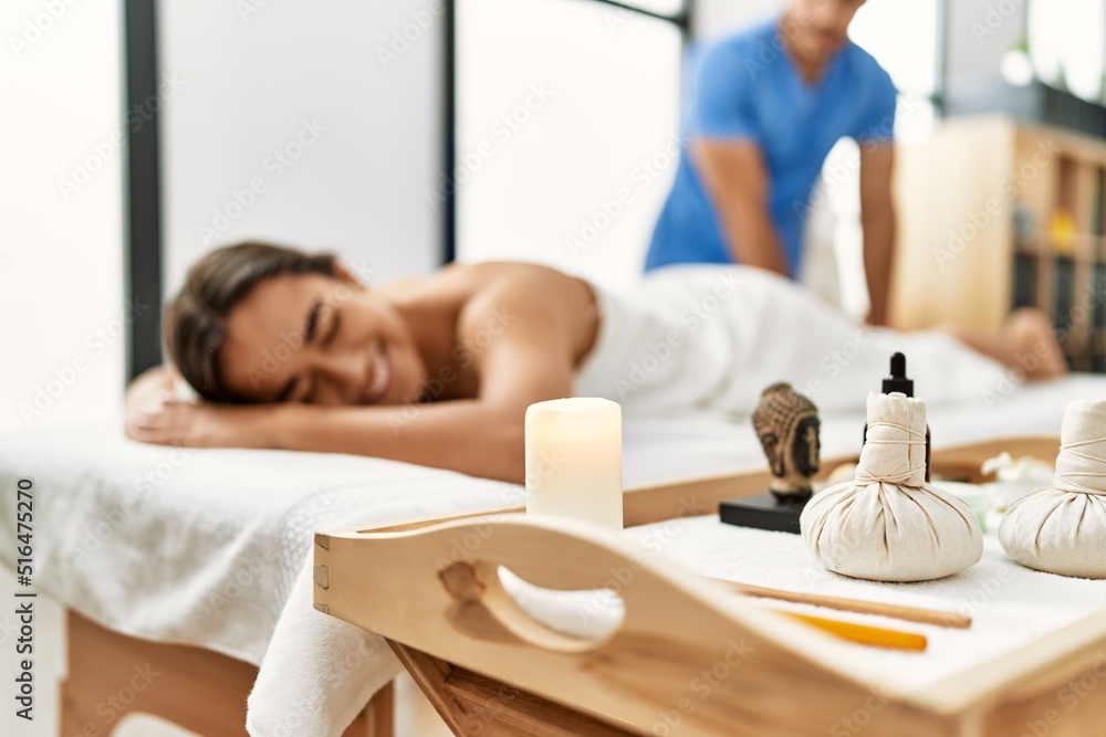 Fototapeta premium Latin man and woman wearing physiotherapy uniform having rehab session massaging legs at beauty center