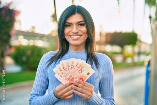 Beautiful hispanic woman smiling confient holding 20 shekels banknotes at the city photo