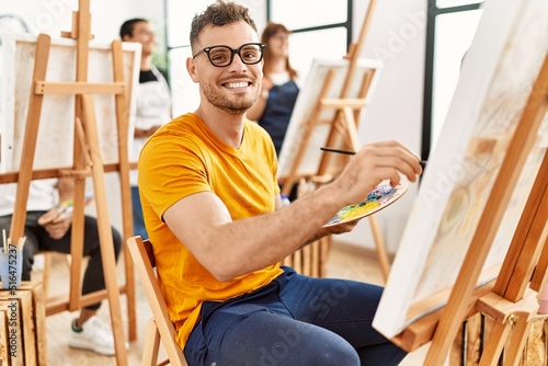 Young man smiling happy drawing with group of people at art studio.