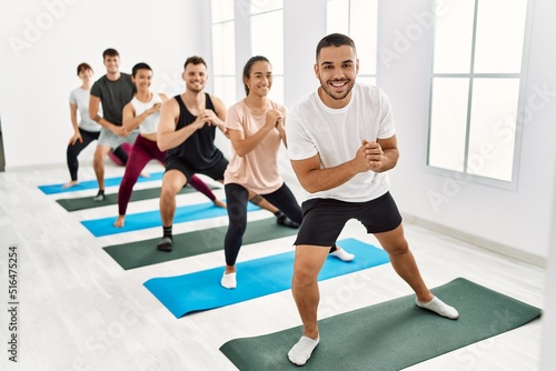 Group of young hispanic people smiling happy training legs exercise at sport center.