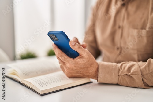Senior man reading book using smartphone at home