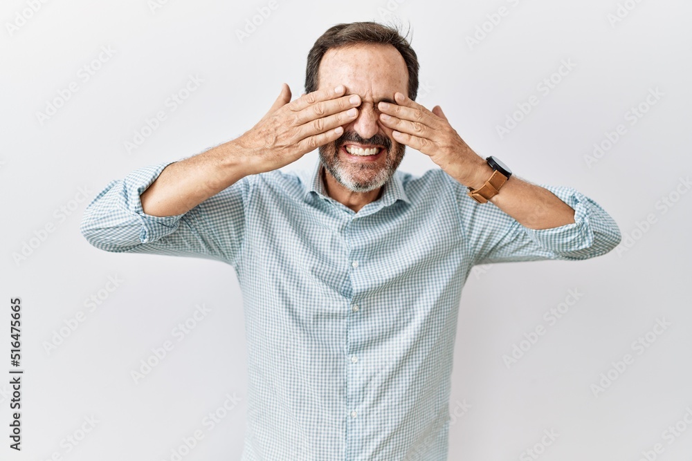 Middle age hispanic man with beard standing over isolated background covering eyes with hands smiling cheerful and funny. blind concept. Middle age hispanic man with beard standing over isolated background covering eyes with hands smiling cheerful and funny. blind concept.