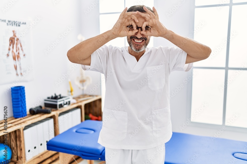Middle age man with beard working at pain recovery clinic doing ok gesture like binoculars sticking tongue out, eyes looking through fingers. crazy expression. Middle age man with beard working at pain recovery clinic doing ok gesture like binoculars sticking tongue out, eyes looking through fingers. crazy expression.