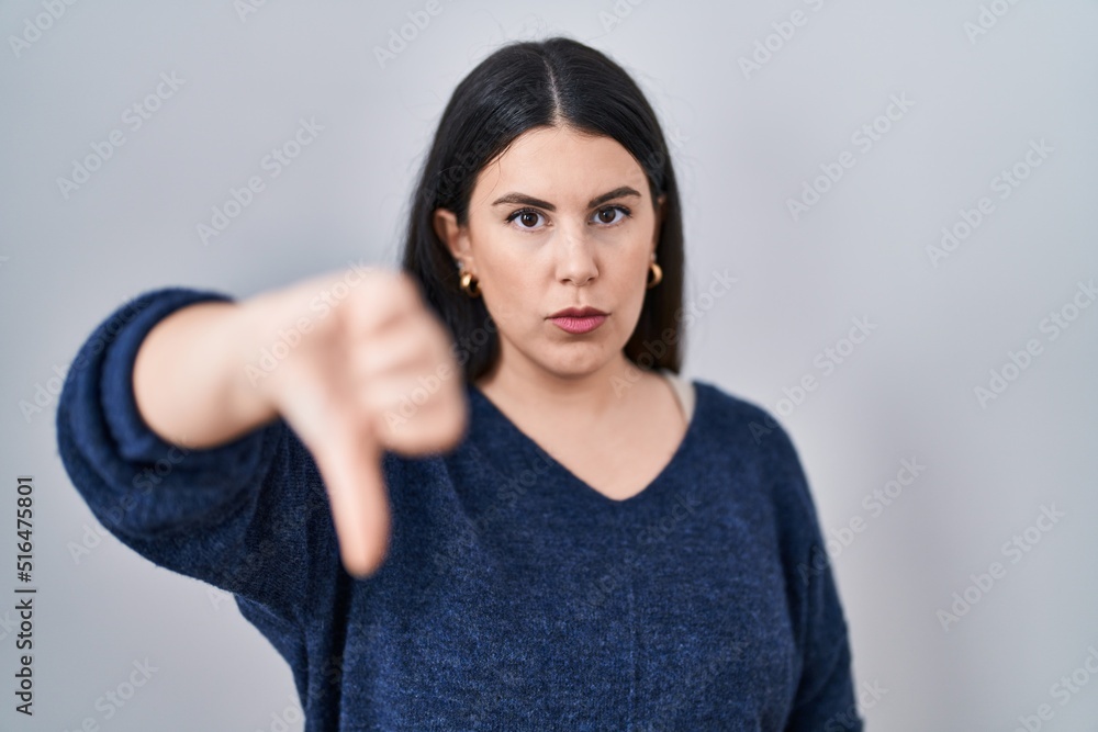 Young brunette woman standing over isolated background looking unhappy and angry showing rejection and negative with thumbs down gesture. bad expression. Young brunette woman standing over isolated background looking unhappy and angry showing rejection and negative with thumbs down gesture. bad expression.