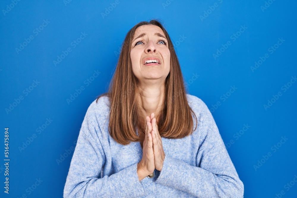 Young woman standing over blue background begging and praying with hands together with hope expression on face very emotional and worried. begging. Young woman standing over blue background begging and praying with hands together with hope expression on face very emotional and worried. begging.