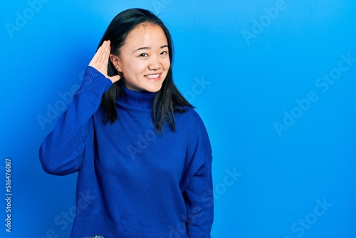 Young chinese girl wearing casual clothes smiling with hand over ear listening an hearing to rumor or gossip. deafness concept. © Krakenimages.com