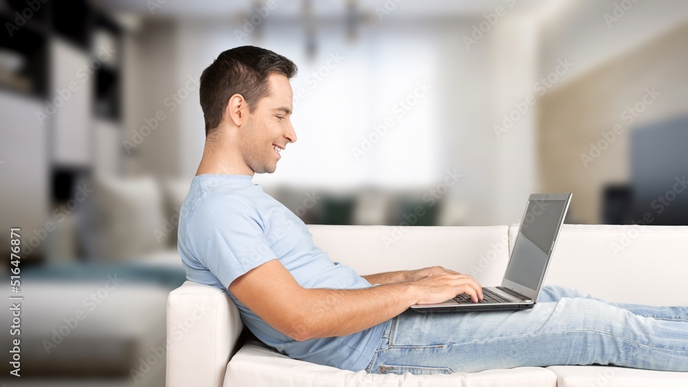 Portrait of smiling man using laptop. Adult male sitting on comfy couch in living room, watching video, taking break Portrait of smiling man using laptop. Adult male sitting on comfy couch in living room, watching video, taking break