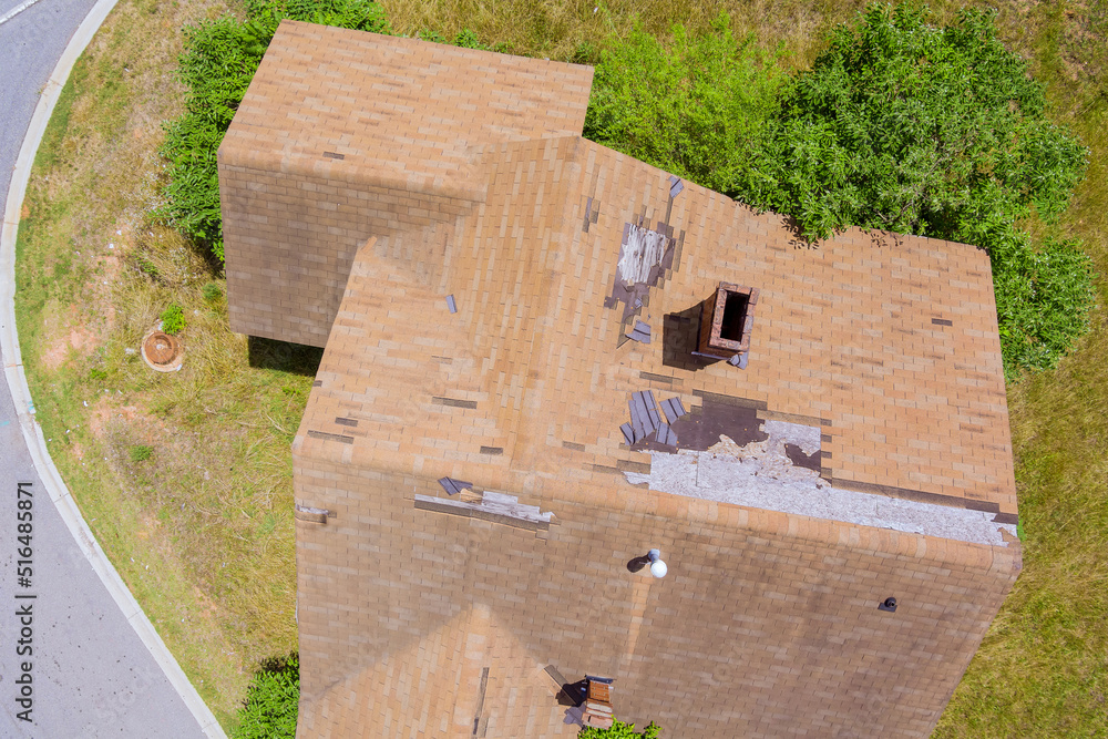 The aerial top view of roof shingles that have been damaged as a result of strong winds and strong storms can be seen below