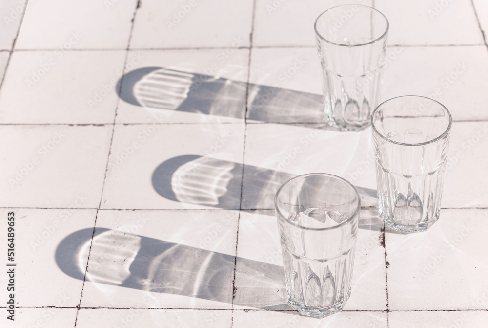 Fototapeta premium glass and sharp shadows stands on a white tiled table. top view of glass