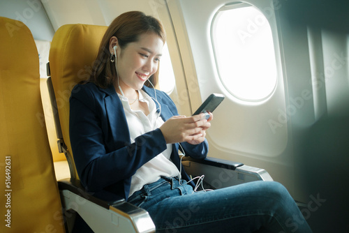 Business woman In a plane, works on using on phone, headphones.