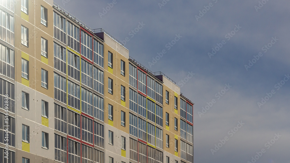 A modern multi-storey panel house in Russia is painted in bright colors against the sky