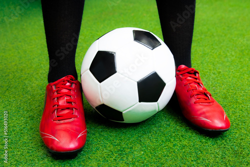 Close up football player with red soccer shoes and black and white ball on artificial grass.