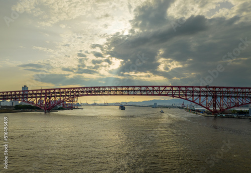 Sun shines through clouds on bridge over river and distant cargo ship