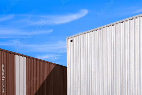 Low angle view of corrugated steel wall of 2 warehouse building against blue sky background in perspective side view © Prapat