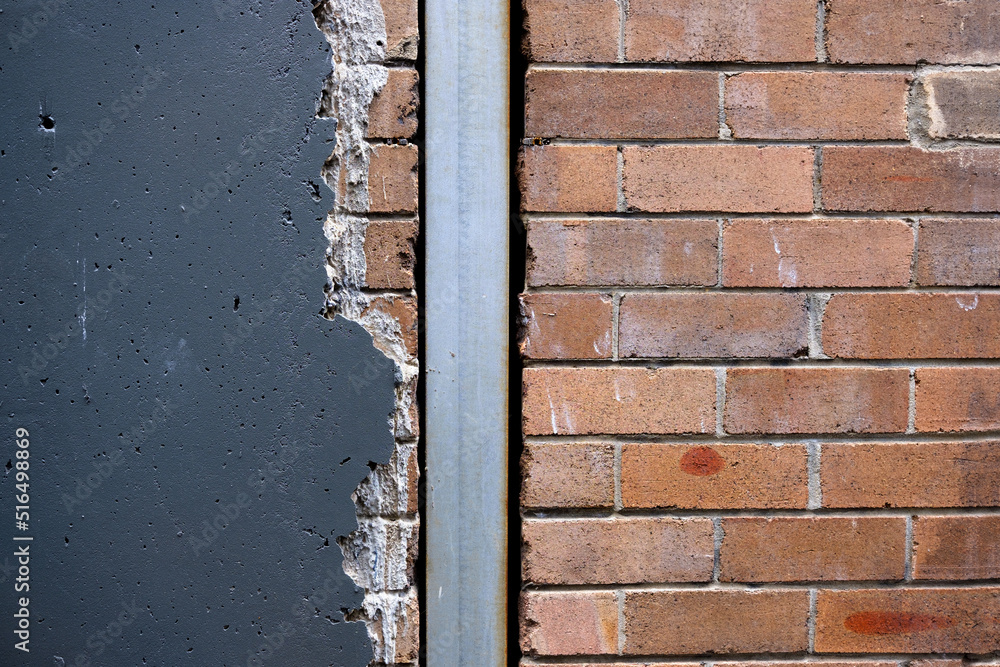 An old exterior brick wall with painted render/stucco cracked away on one side, with a rainwater down pipe running through it. An old exterior brick wall with painted render/stucco cracked away on one side, with a rainwater down pipe running through it.