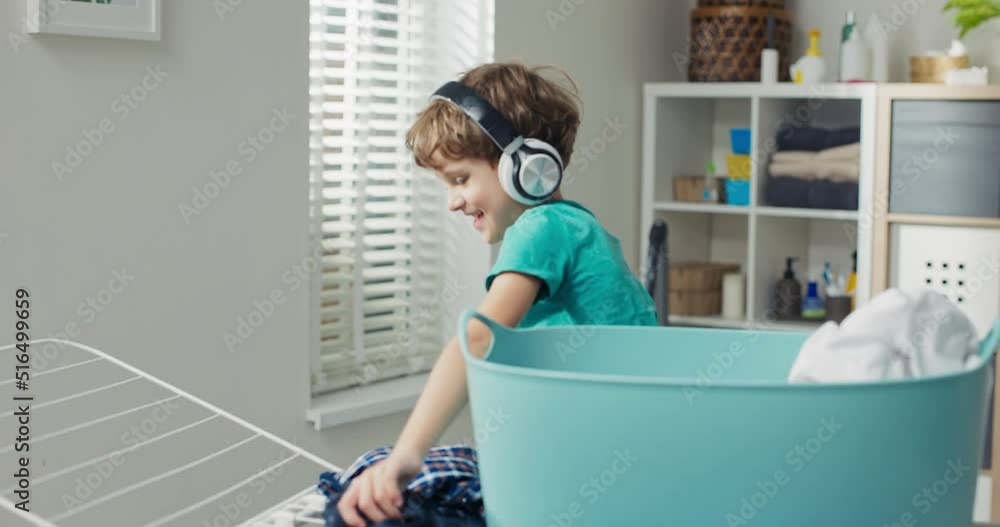 Boy with curly hair wearing wireless headphones stands by clothes dryer