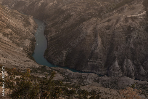 Mountain landscape with canyon view - steep slopes and thin blue river in golden sunlight on sunset, hight view in precipice.Wondering adventure, tourism and travel on Caucasian ridge in Dagestan.