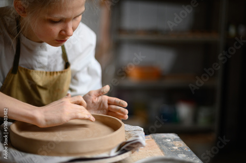 A ceramist makes a plate. Woman in an apron works in a pottery workshop. 