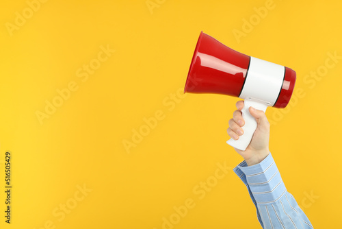 Female hand holds megaphone on yellow background