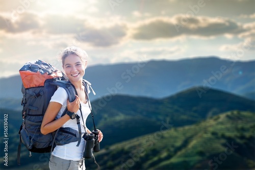 Portrait of a smiling woman relaxing during a mountain hike. Female with backpack enjoying the view while standing on the top of the mountain.