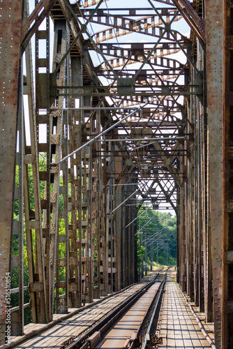 The metal structure of the railway viaduct over the river against the background of a blue sky with clouds.