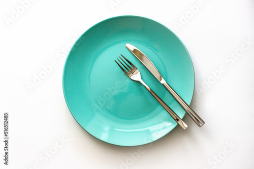 Served plate with cutlery. Empty green plate and stainless knife and fork isolated on white background. Top view.