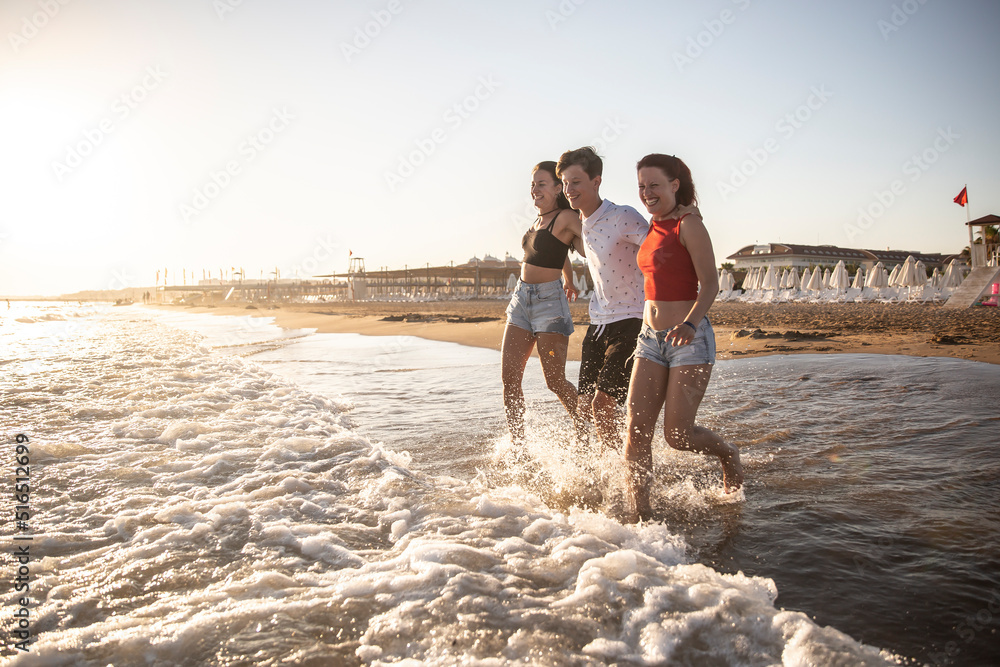 Three siblings enjoy their vacation by the sea and run into the sea at sunset