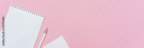 Workspace concept for school or office. Flat lay with an open notebook on a spring, a white color pencil, a plastic clip on paper background colors pink with copy space.