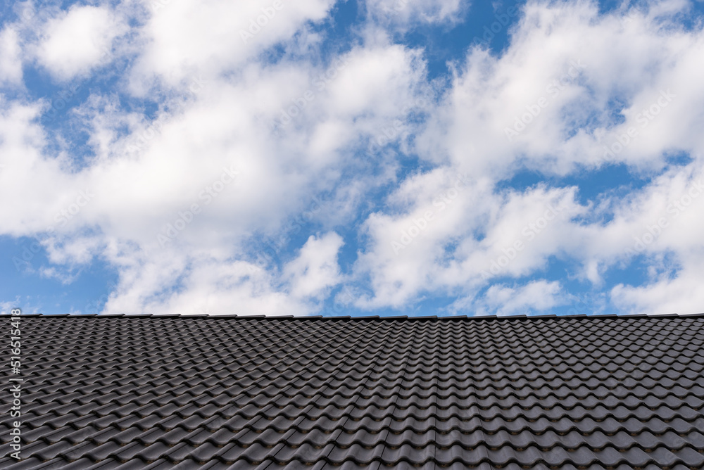Black tile roof against blue sky with white clouds. Black tile roof against blue sky with white clouds.