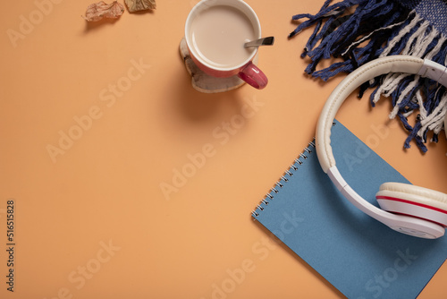 Table with blue paper note pad, coffee cup, headphones and pliad on colored background. Top view photo