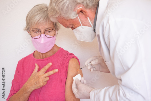 Doctor giving injection to senior caucasian woman, female receiving third booster of covid 19 vaccine, people wearing mask