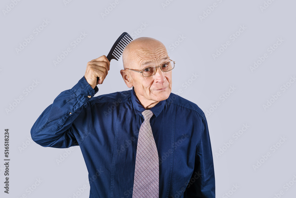 Naklejka premium Strange mature man holds hair brush on bald head. Male alopecia problem.