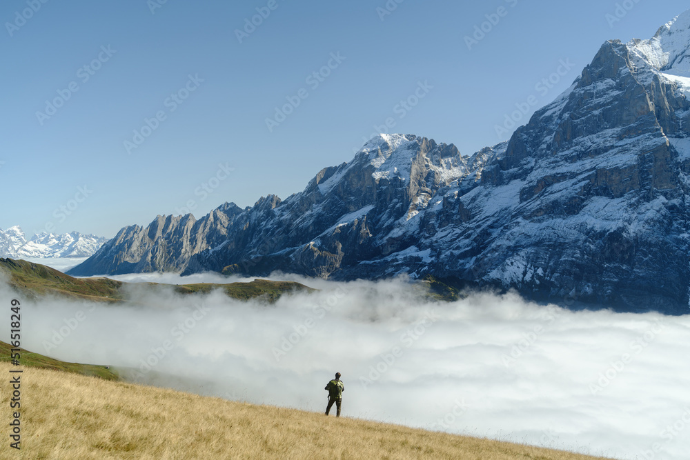 Tourist stands in front of the mountains and clouds in the valley at Grindewald, Switzerland.