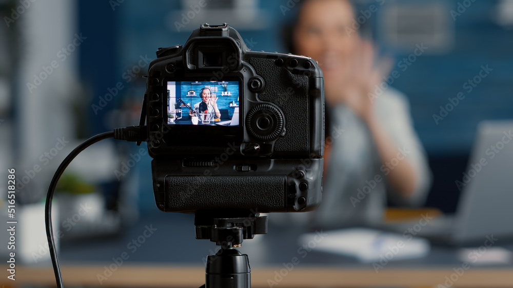 Modern camera filming influencer talking to audience. Popular social media content creator recording vlog for internet video sharing platforms while sitting at studio desk. Close up