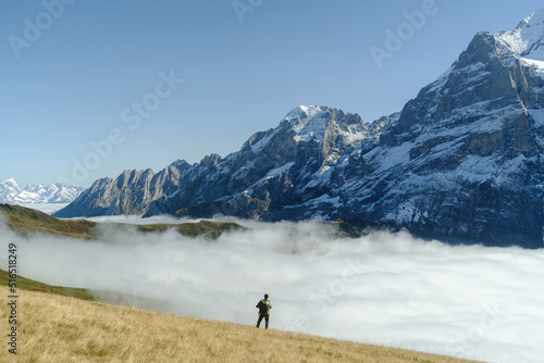 Tourist stands in front of the mountains and clouds in the valley at Grindewald, Switzerland. © Anton Zabielskyi