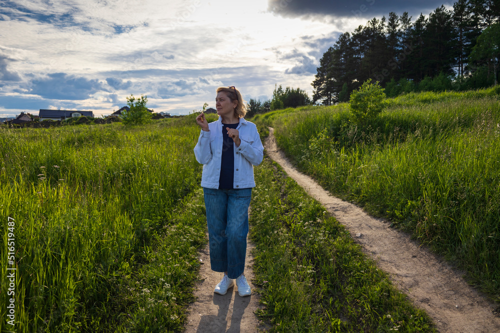 An adult woman enjoys the beauty of nature, walking along a rural road in summer.