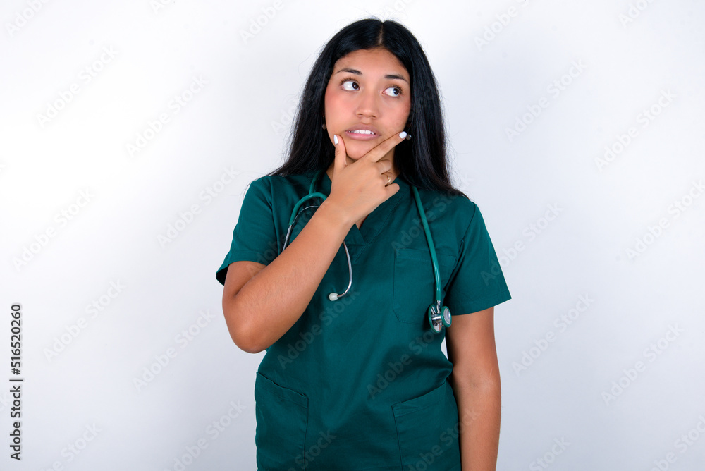 Doctor hispanic woman wearing surgeon uniform over white wall Thinking worried about a question, concerned and nervous with hand on chin. Doctor hispanic woman wearing surgeon uniform over white wall Thinking worried about a question, concerned and nervous with hand on chin.