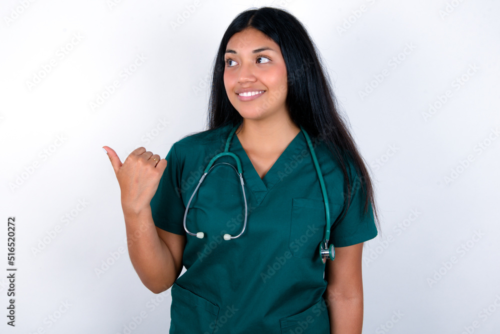 Charming Doctor hispanic woman wearing surgeon uniform over white wall looking at copy space having advertisements Charming Doctor hispanic woman wearing surgeon uniform over white wall looking at copy space having advertisements